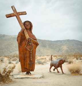 metal sculpture  Father carrying a cross with a dog and a bone